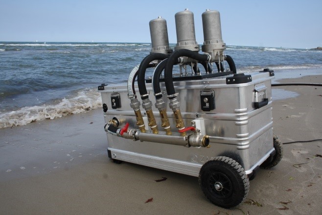 Seitenansicht der ‚Rocket‘. In einer Aluminium Box befindet sich die Pumpe, um Wasser über die Filter anzusaugen. Die vier Kerzenfilter befinden sich jeweils in einem Edelstahl Gehäuse und sind senkrecht auf der Box angebracht. Sie sind über Schläuche mit der Pumpe und dem Einlassschlauch verbunden.